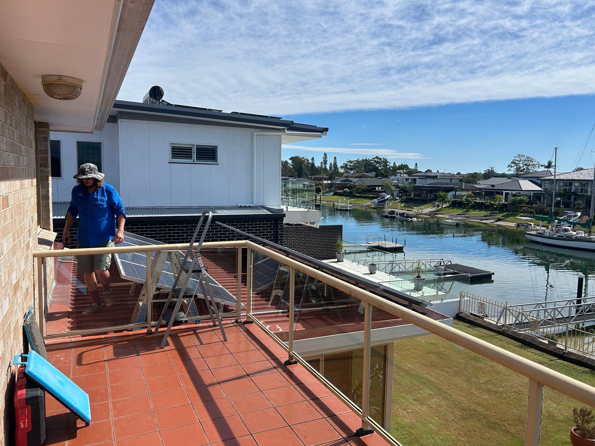 Worker on red deck by waterfront, with boats and a white building under a blue sky.