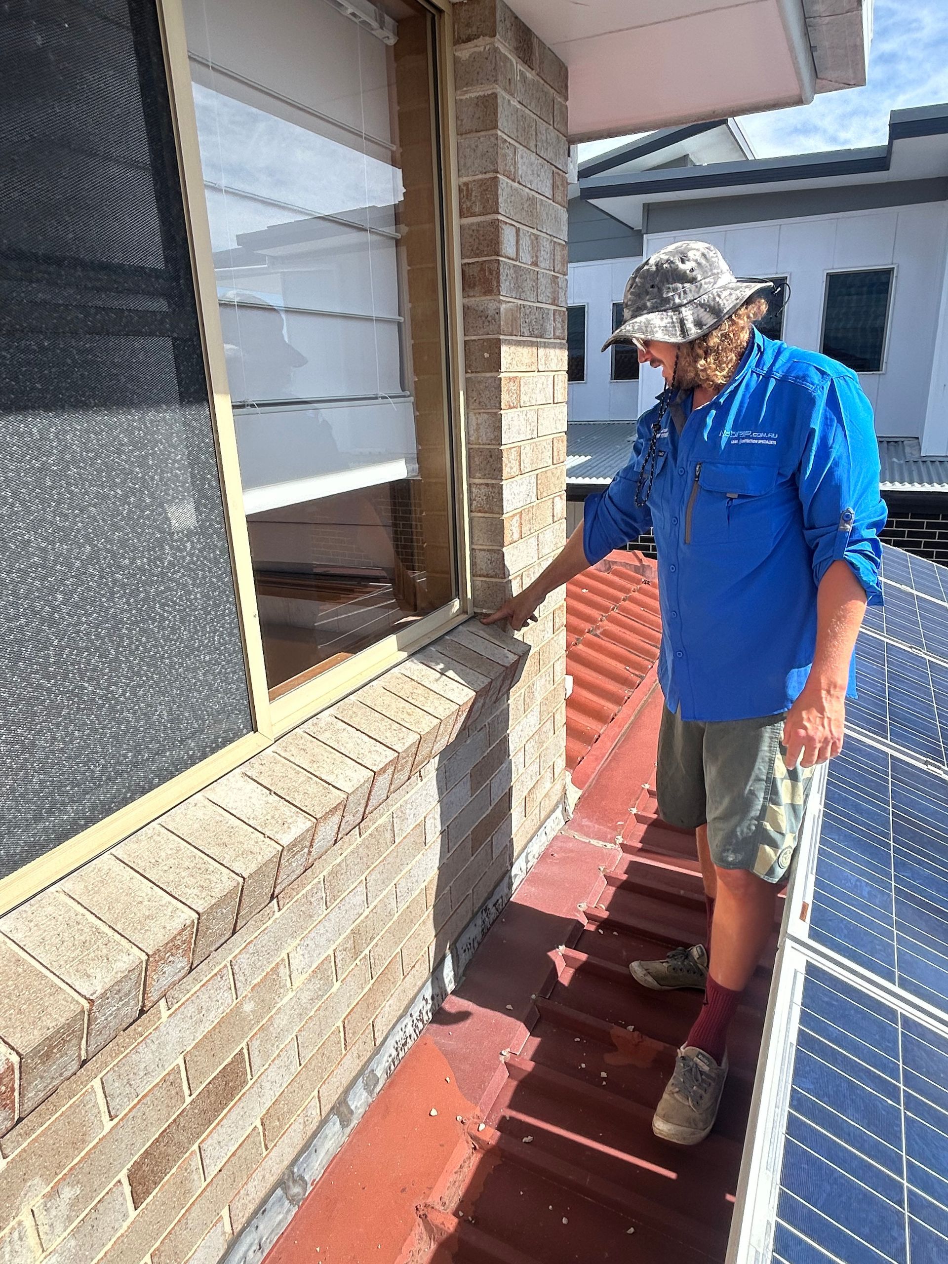 Person in blue shirt inspecting a brick exterior wall beside a red walkway