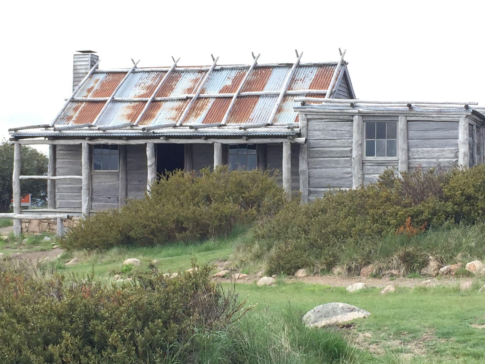 Weathered old wooden cottage with a rusty roof, surrounded by grass and shrubs.