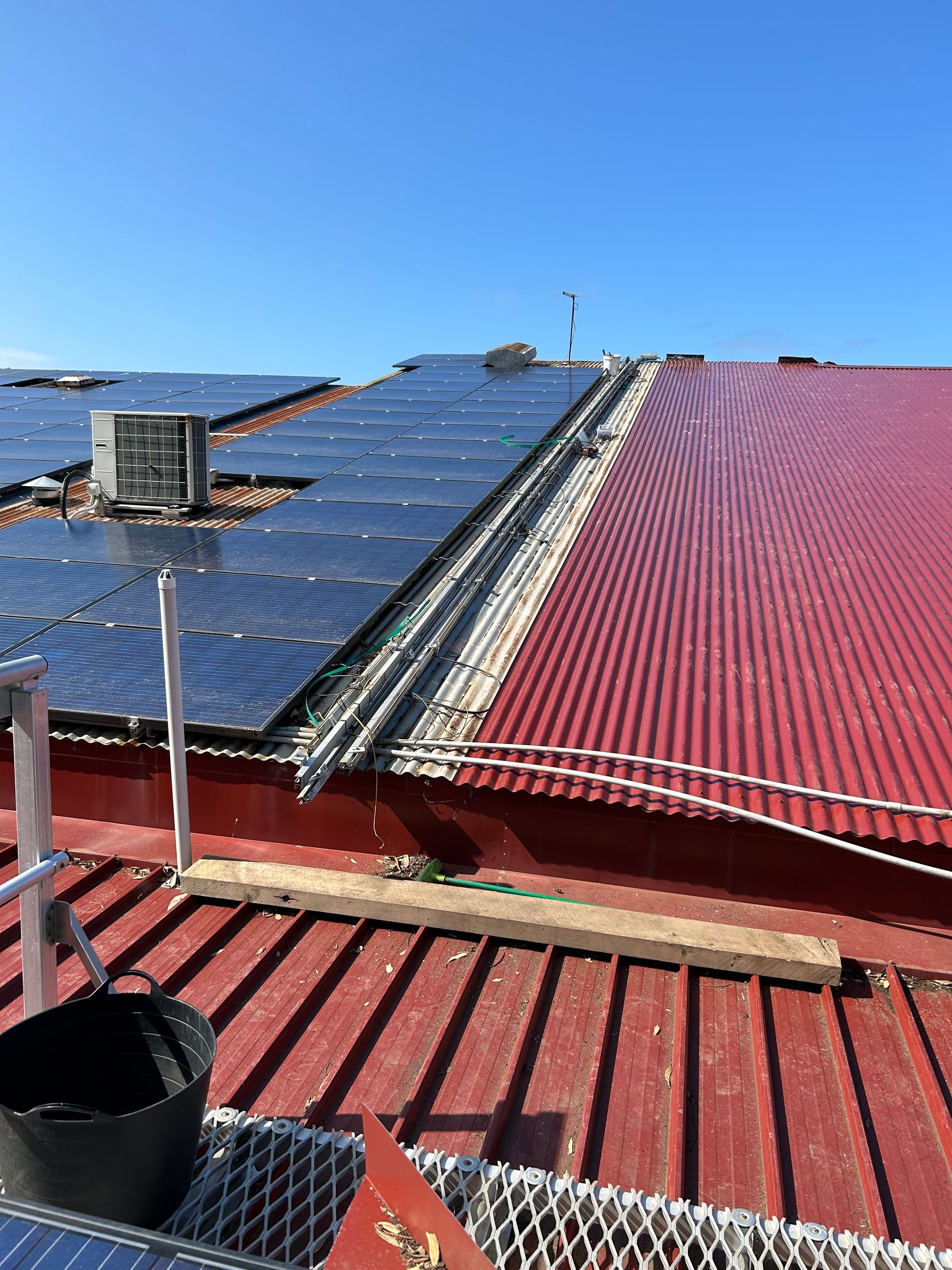 Rooftop with red metal panels and solar panels under a clear blue sky, overlooking the sea