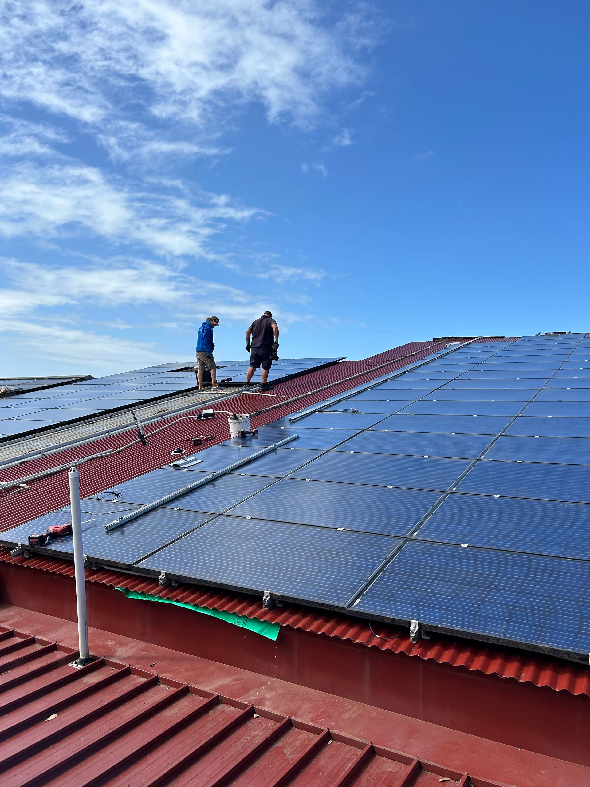 Two workers on a rooftop beside rows of solar panels under a blue sky