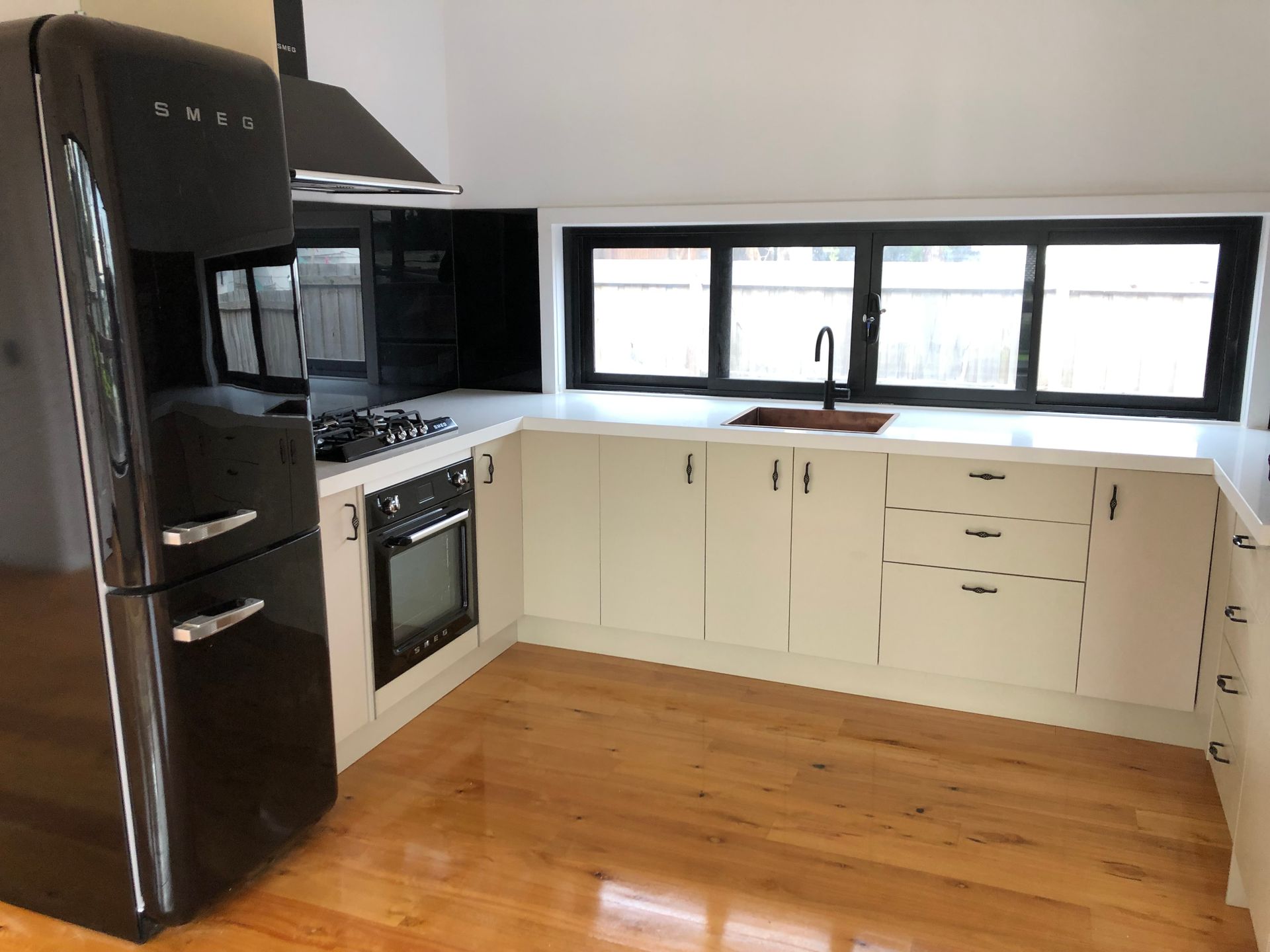 Modern kitchen with black appliances, white cabinets, wood floor, and large window above the counter