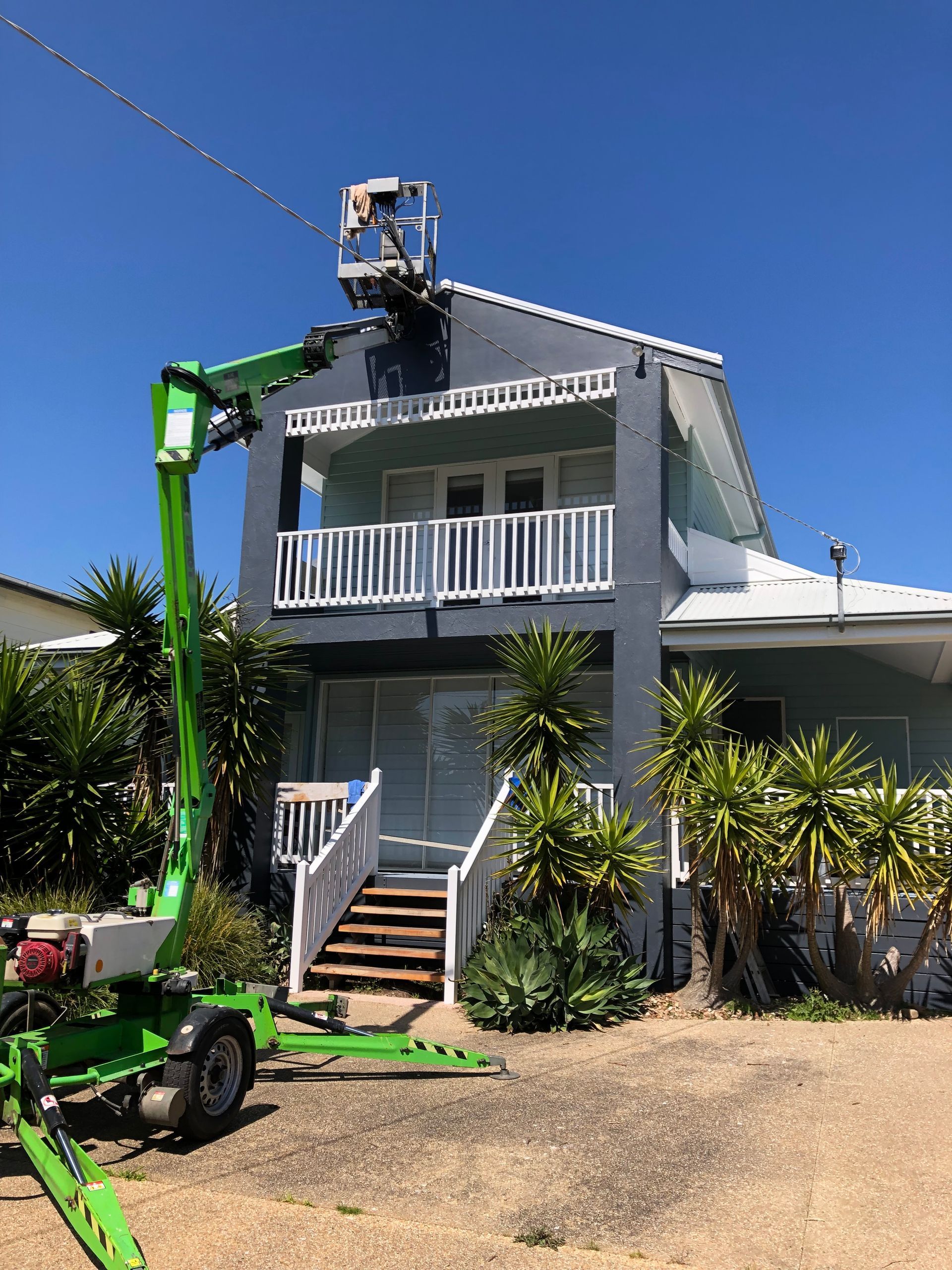 House exterior with a worker on a lift trimming the roof, and a small green utility cart in front