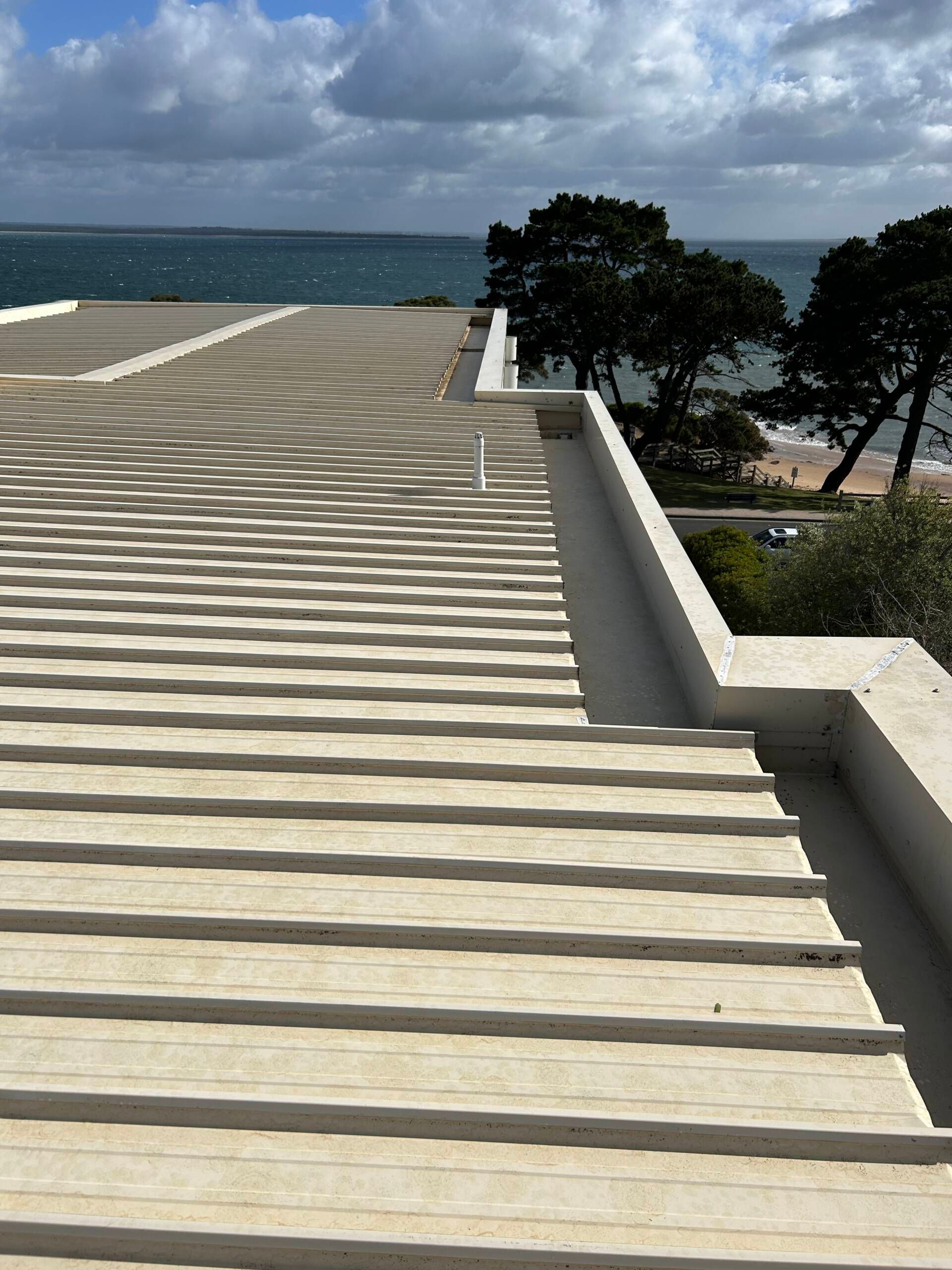 Wide concrete steps leading to the sea, with trees and shoreline on the right under a cloudy sky.