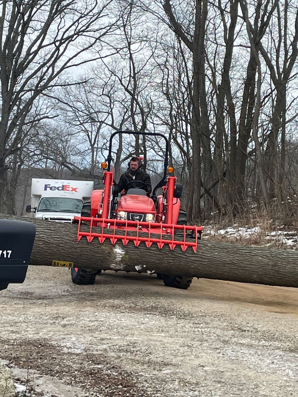 A man is driving a tractor arrying a large tree trunk.