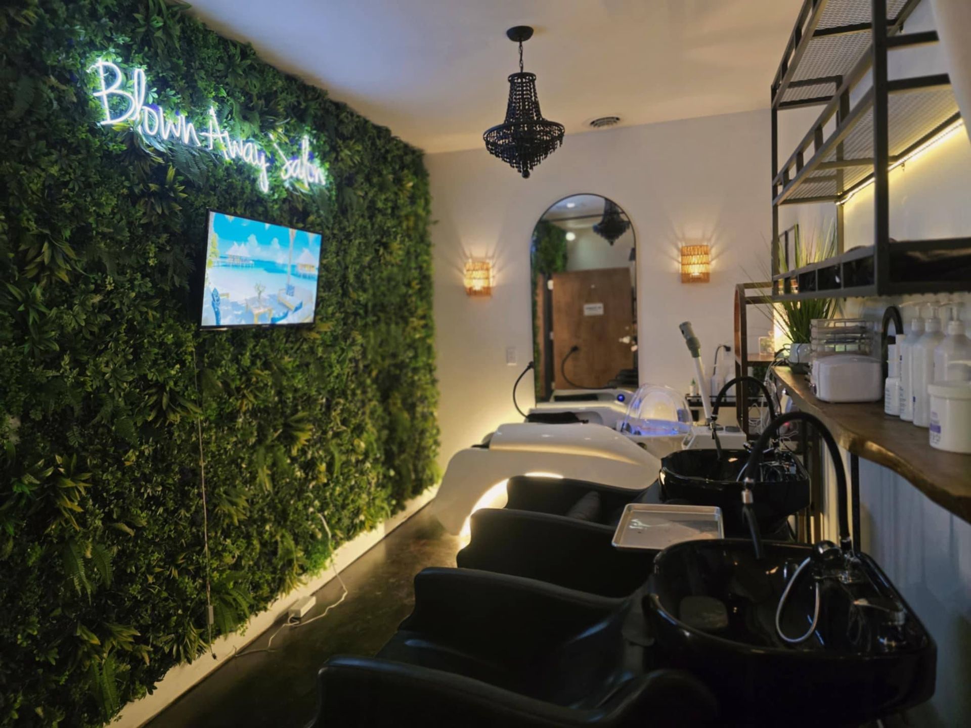 Hair salon interior with green wall, washing stations, mirrors, and black chairs.