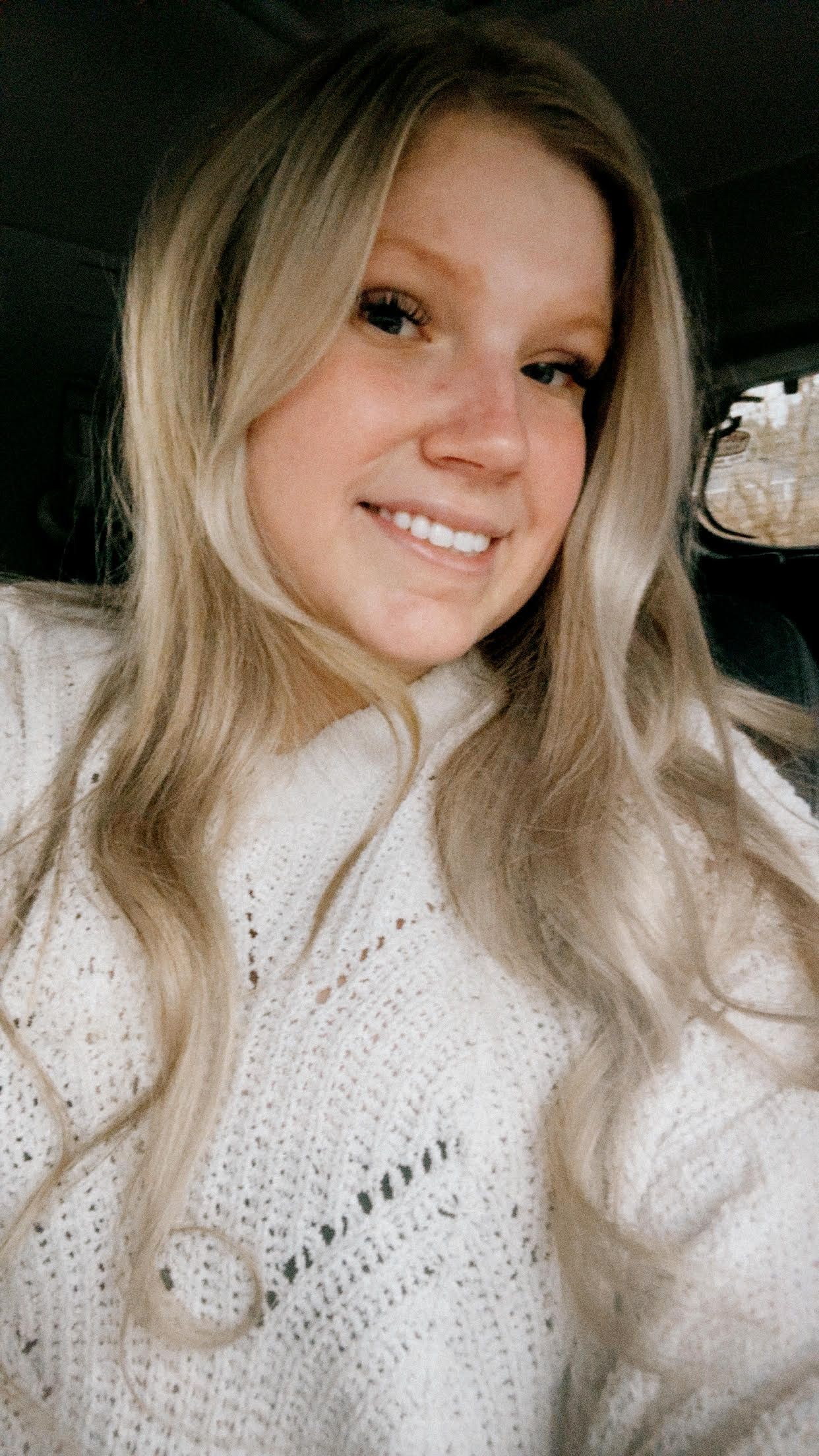 Blond-haired person smiling, wearing a cream-colored sweater.