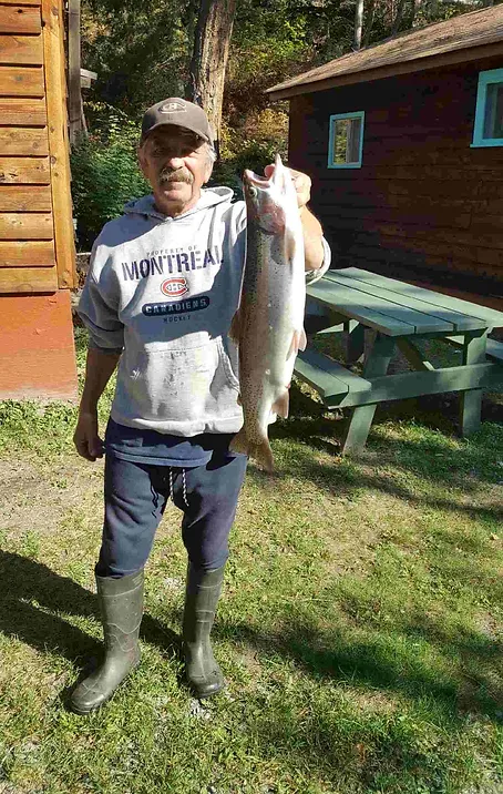 A man is holding a large fish in front of a picnic table.