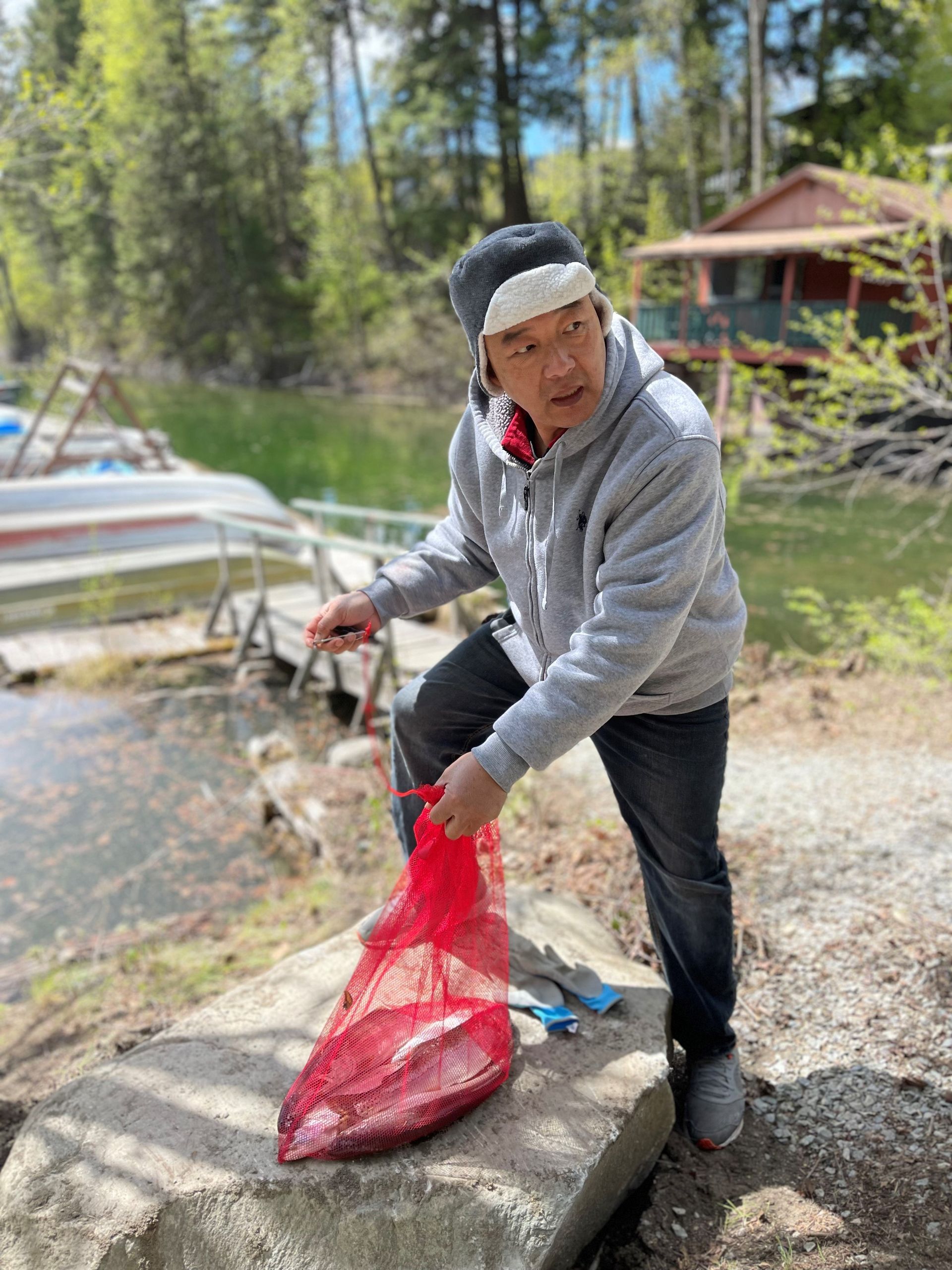 A man is kneeling on a rock next to a bag of fish.