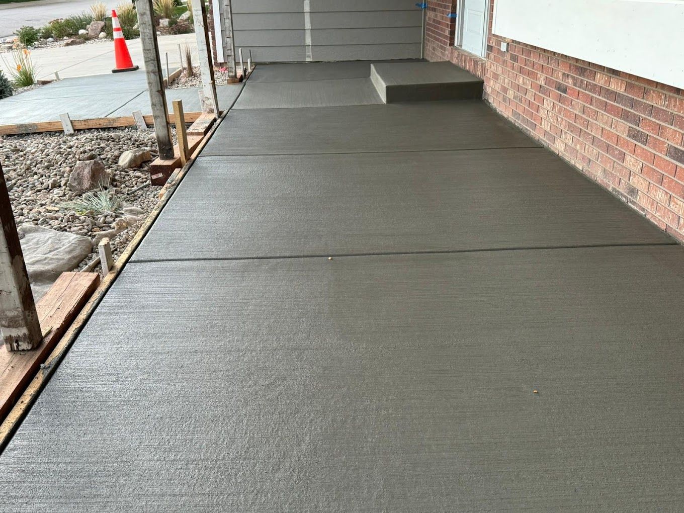 Freshly poured concrete walkway and step in front of a brick building and garage.