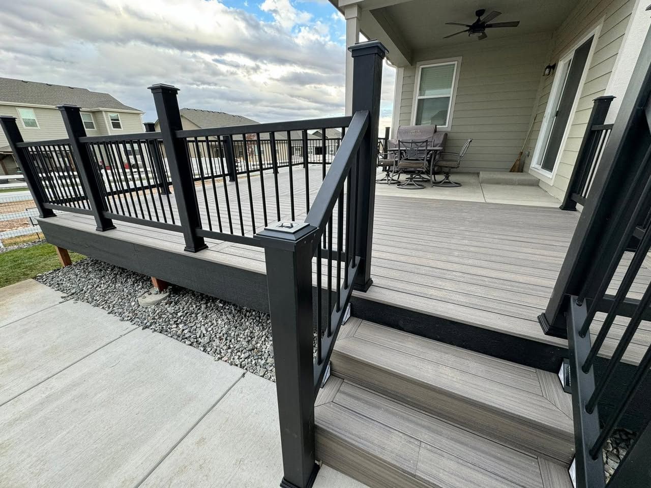 Black railing and steps leading to a gray composite deck, next to a home with a light-colored exterior.