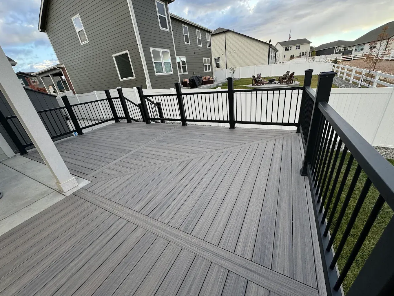 Grey composite deck with black railings and decorative white fence in a backyard setting.