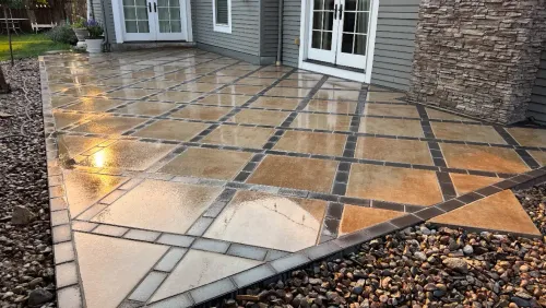 Wet stone patio with patterned tiles, next to a building and gravel.