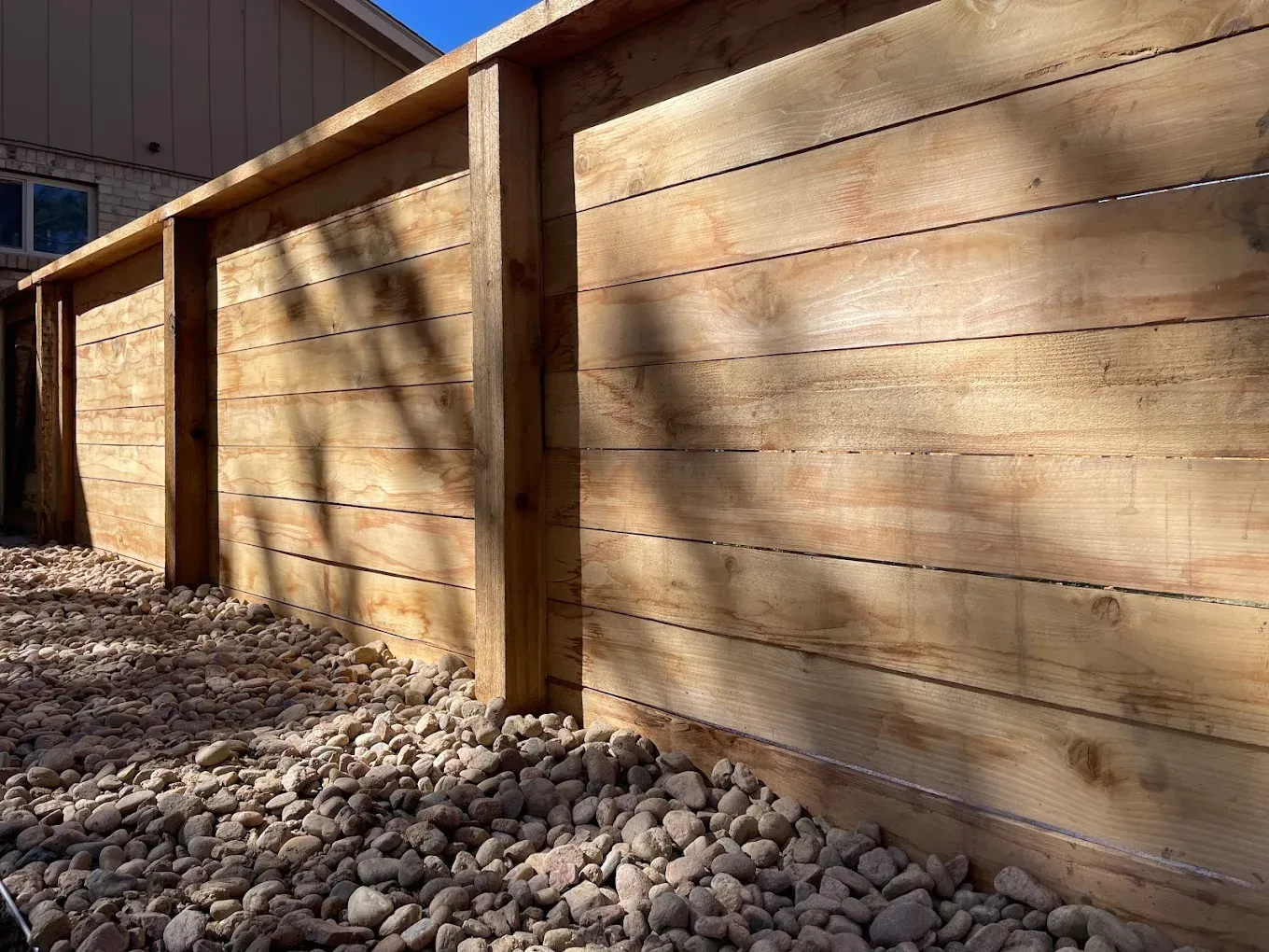 Wooden retaining wall with gravel base, sunlight casting shadows.