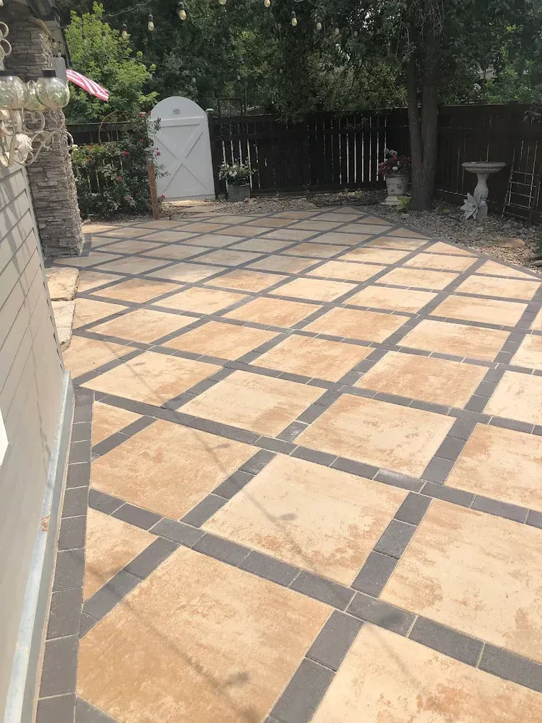 Patio with tan and dark tile pattern, bordered by a beige wall and dark fence.