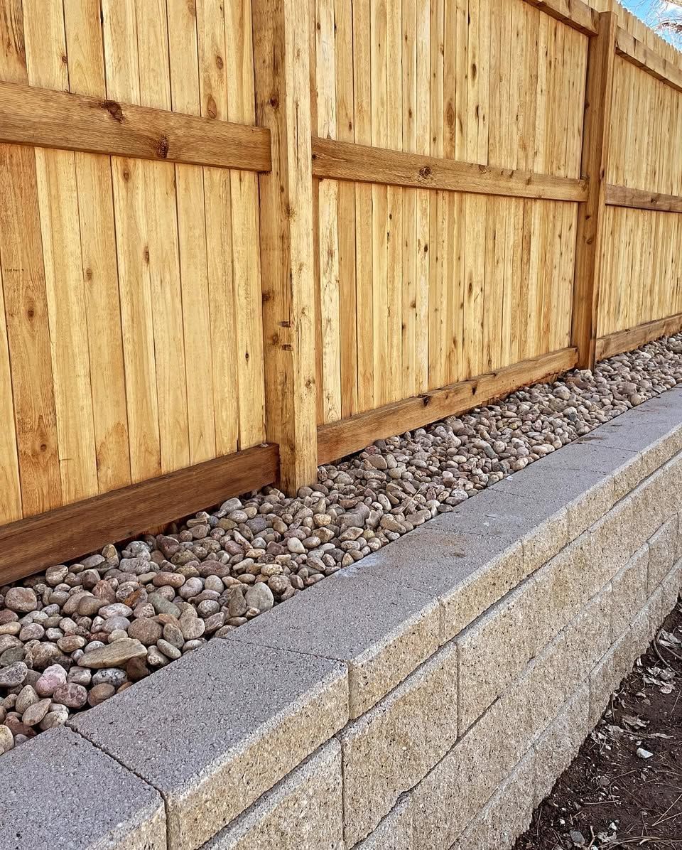 Wooden fence with stone retaining wall and gravel bed.