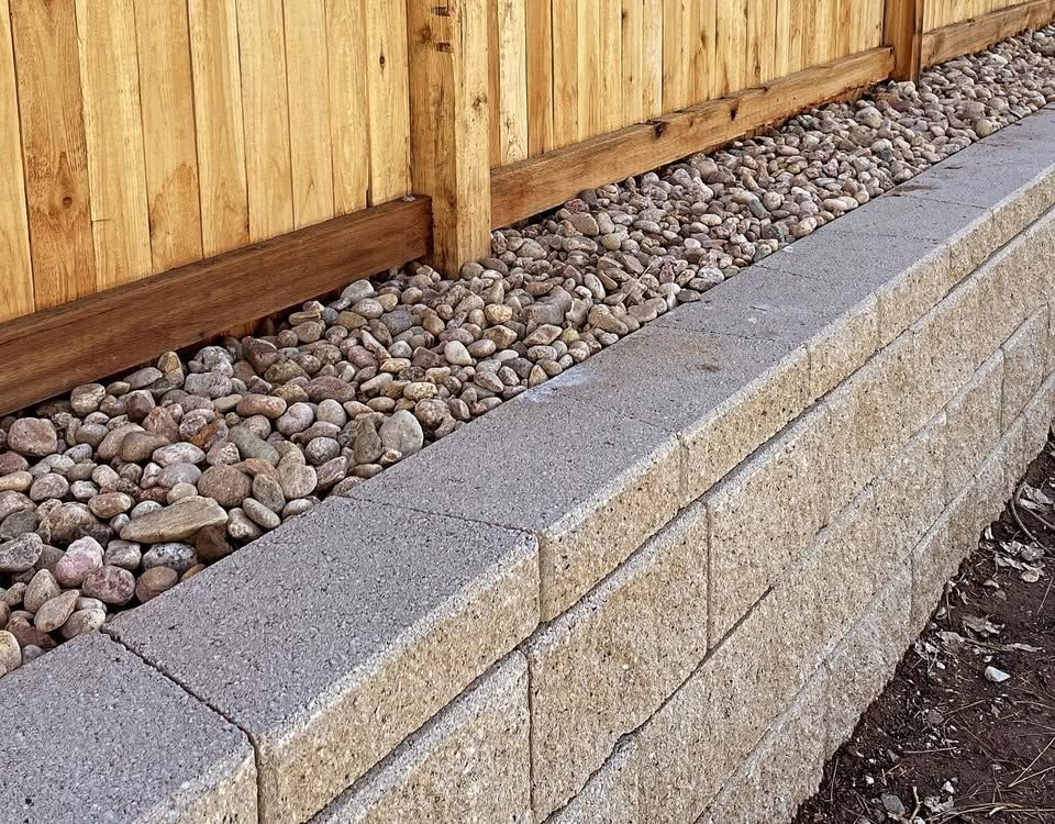 Stone retaining wall with gravel base beneath a wooden fence.