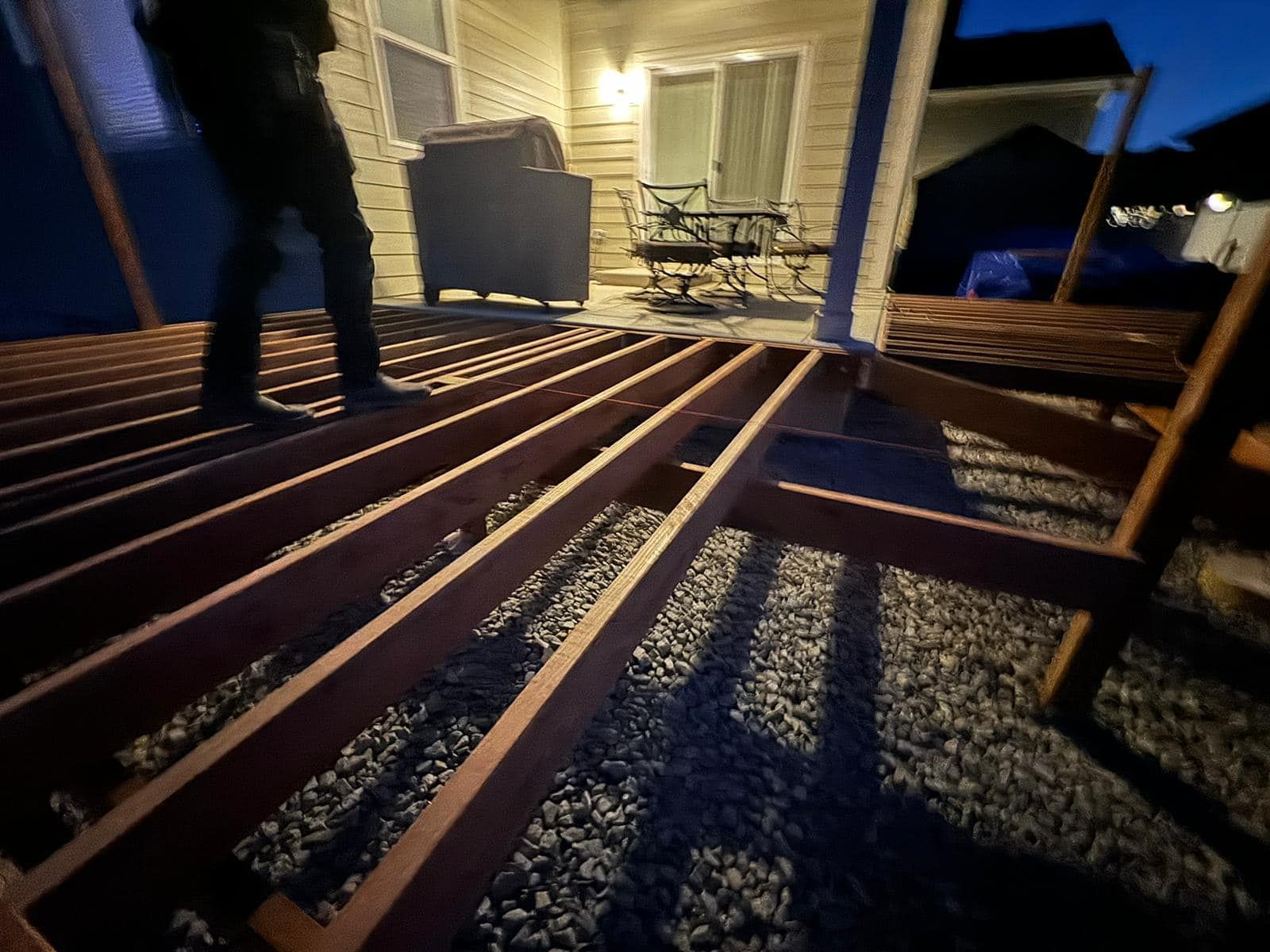 Person standing on unfinished wooden deck, gravel below, evening setting.