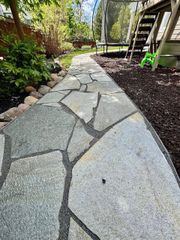 Stone path in a backyard with wood chips and a wooden playset in the background.