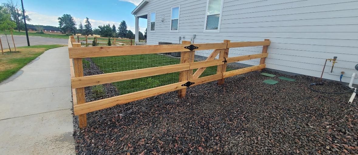 A wooden fence encloses a small yard next to a house with gravel ground covering.