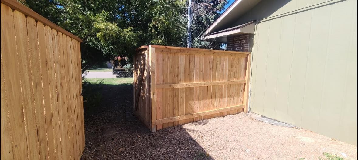 Wooden fences enclose a narrow area next to a house with trees in the background.