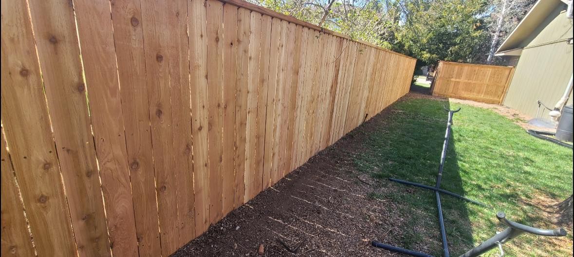 Wooden fence along a yard with mulch on one side and grass on the other.