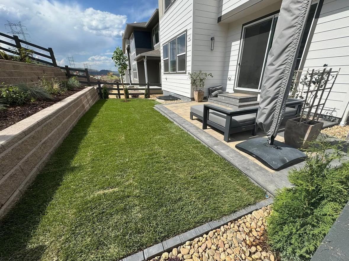 Backyard with green lawn, patio furniture, and retaining wall.