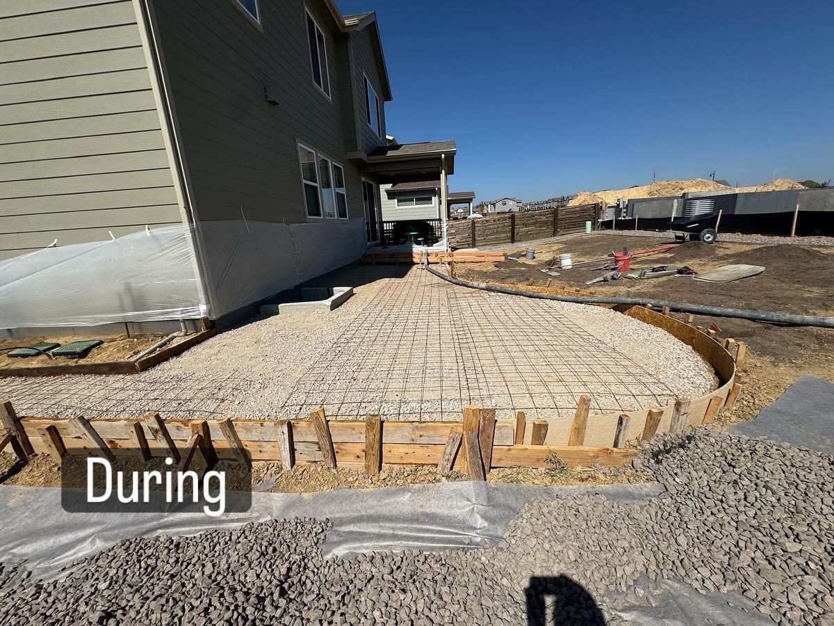 Construction site; concrete slab foundation being built next to a house with gravel and wooden forms.