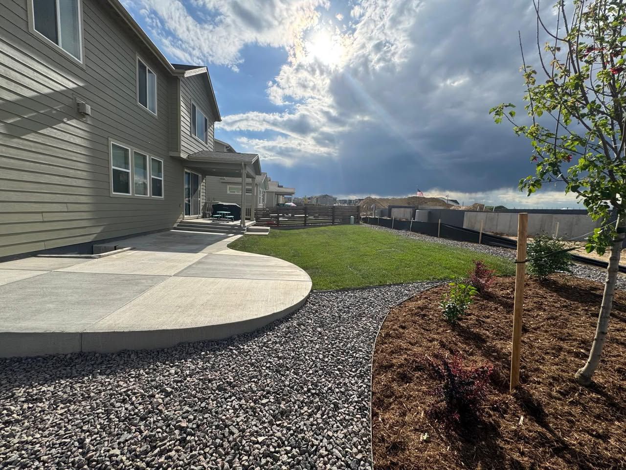 Backyard with a concrete patio, green grass, and a sunny, cloudy sky.