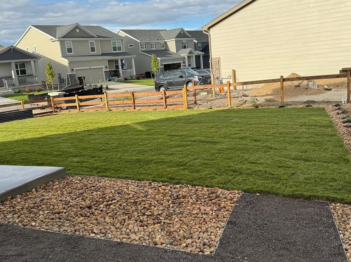 Lawn and gravel yard with a small wooden fence, and houses in the background.