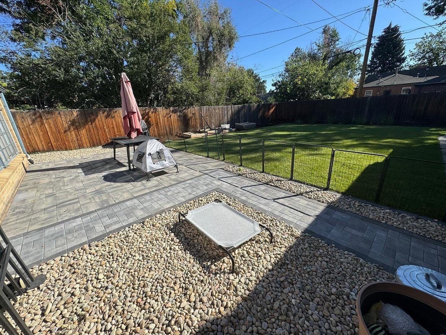 Backyard patio with gravel, pavers, lawn, fence, and a dog bed.