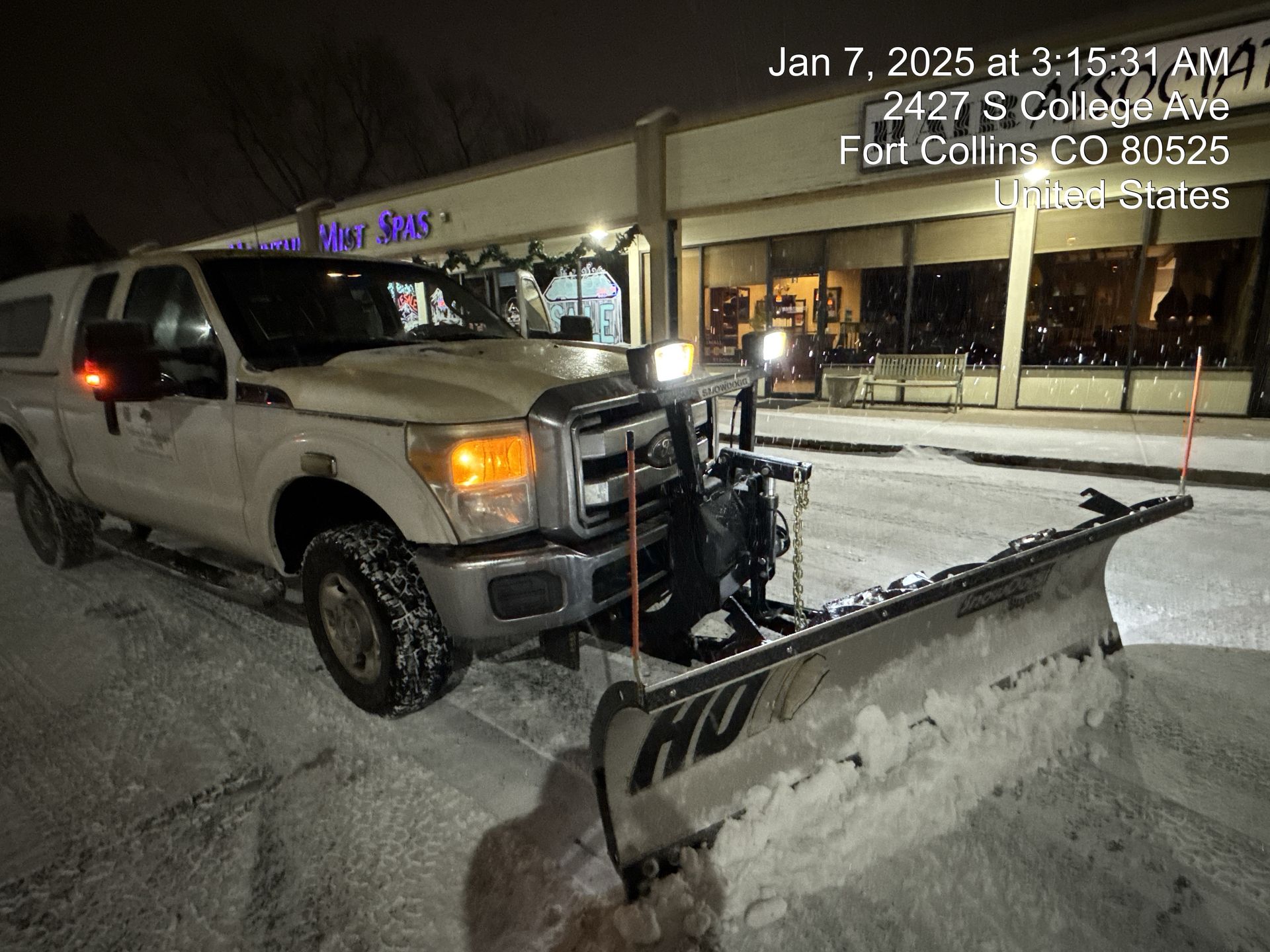 Snowplow clearing snow at night in Fort Collins, CO. The plow has a large blade.
