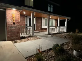 Brick home with a covered porch at night. The porch has white railings and a wooden ceiling. The front walk is concrete.