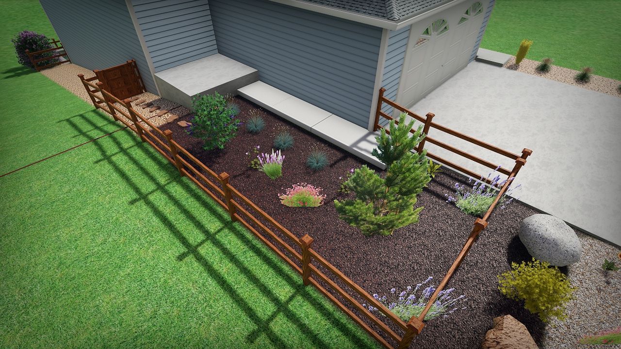 Brown wooden fence bordering a landscaped garden bed with various plants and mulch next to a house with a concrete driveway.