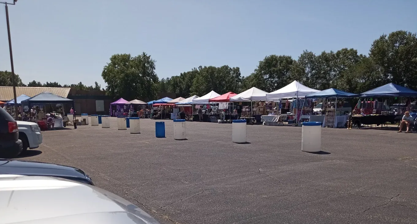 An outdoor market set up in a parking lot on a sunny day. White tents line the space with customers.