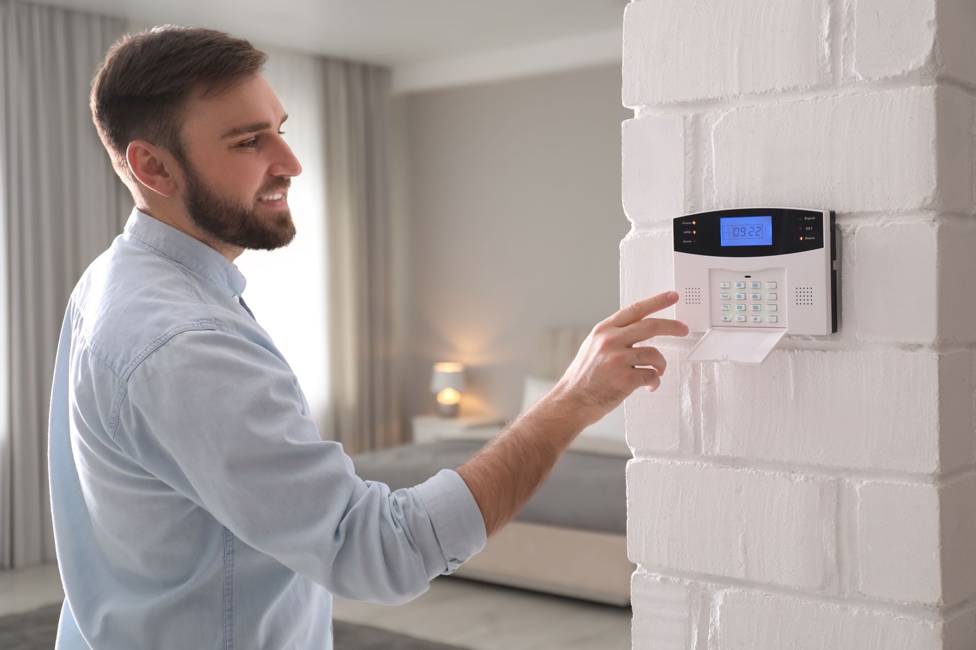 A smiling man is entering code on the security alarm system at home.