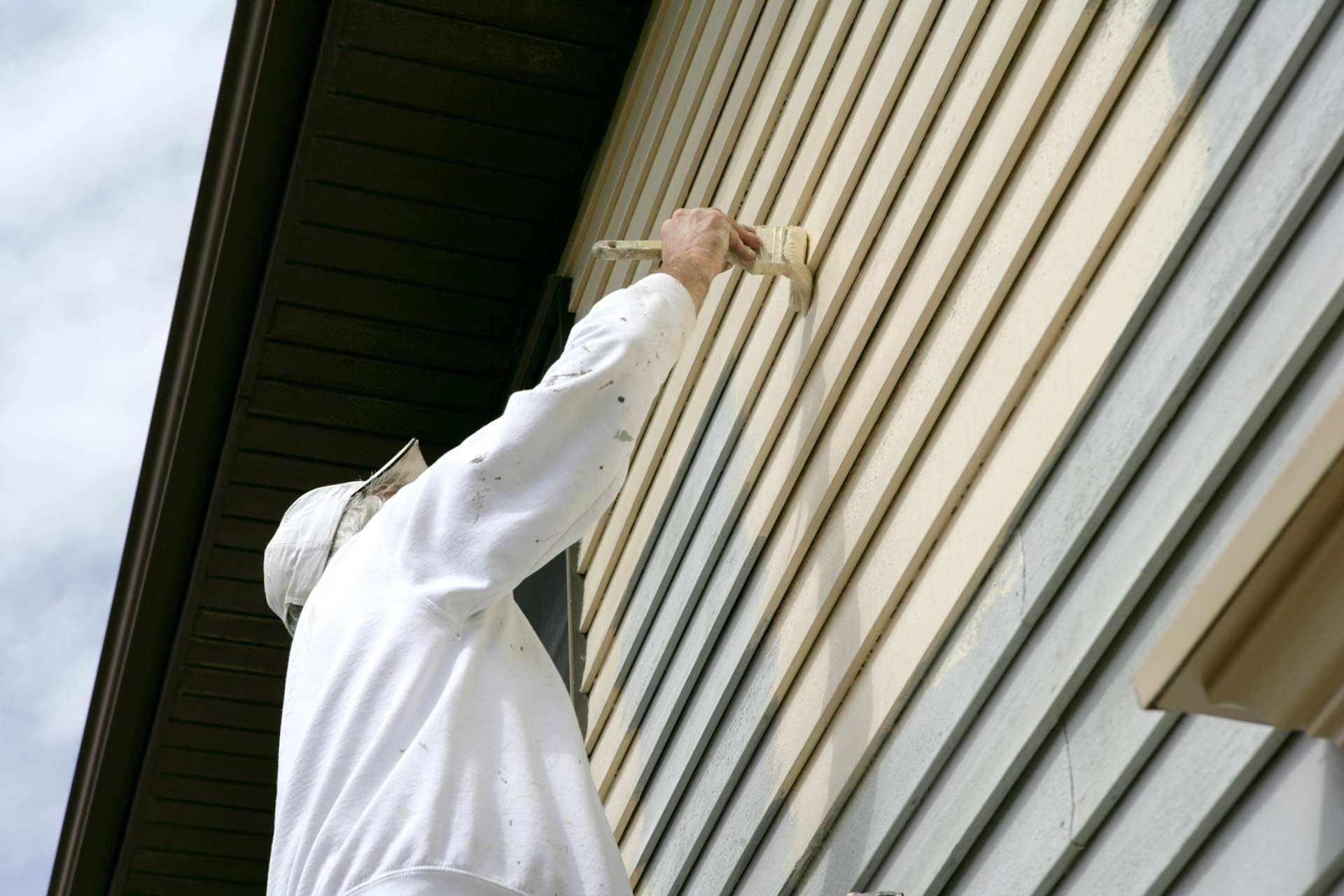 A man is painting the side of a house with a brush