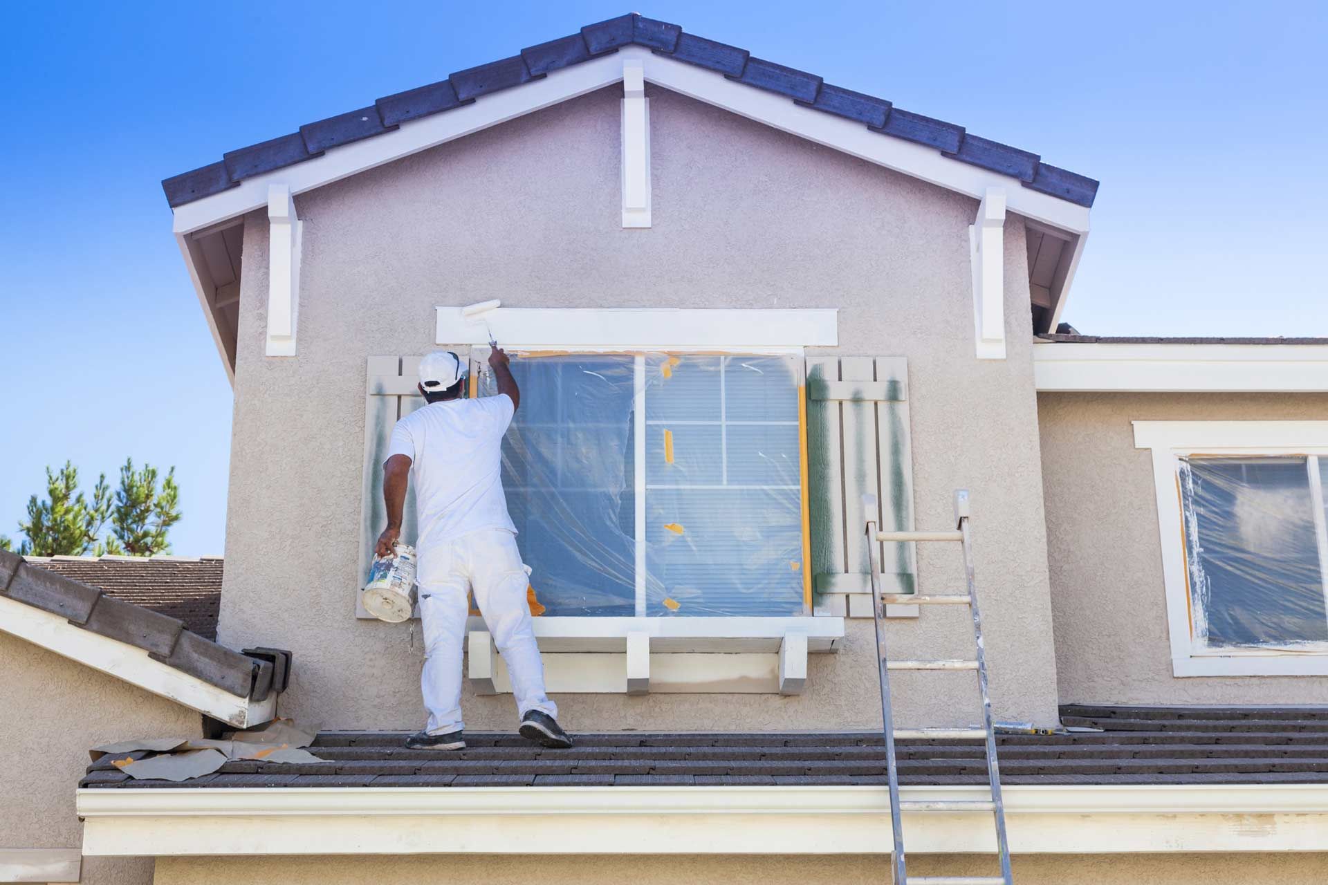 A man is painting a window on the side of a house