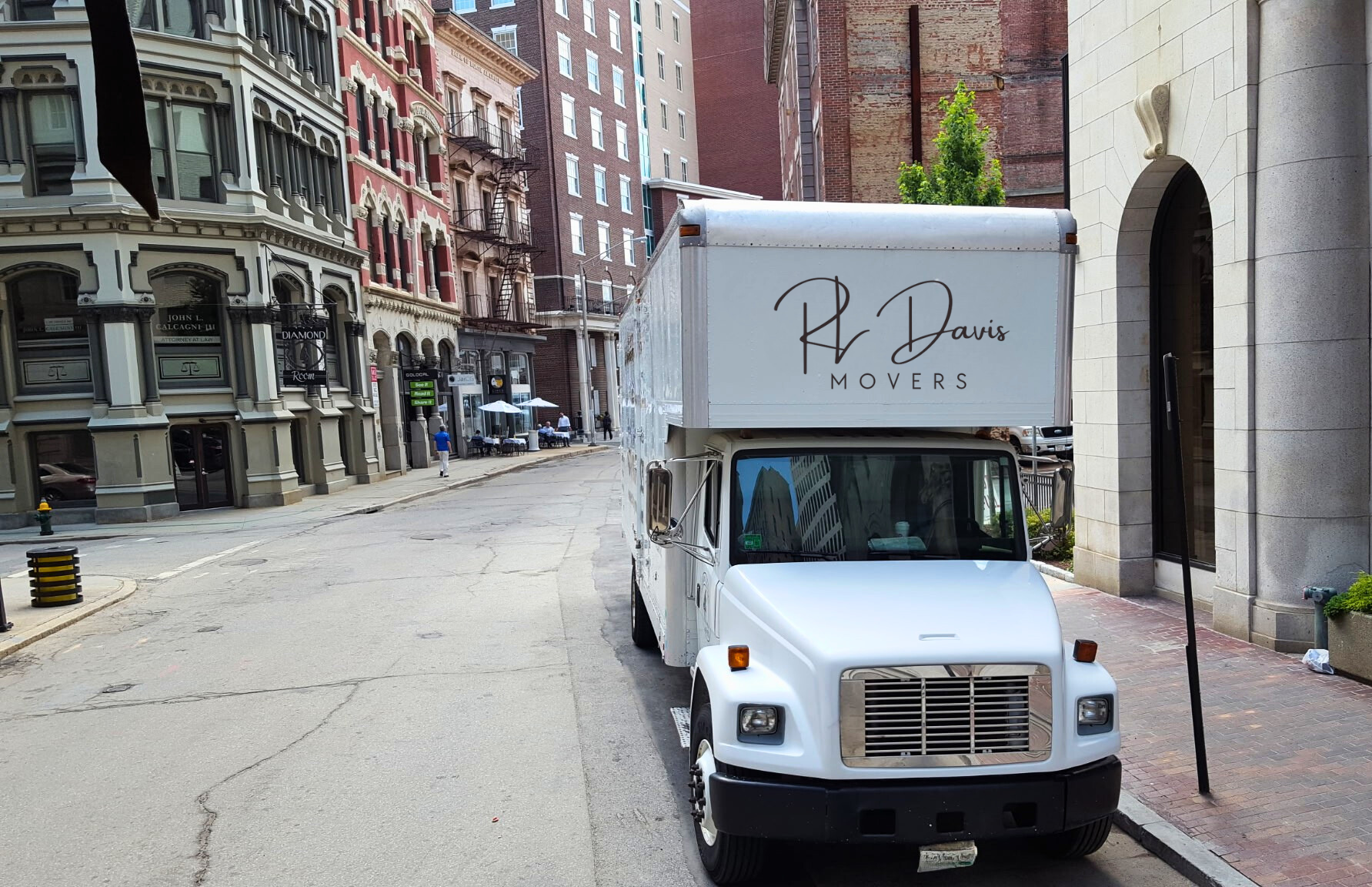 White delivery truck parked on a city street. Buildings with ornate facades line the road.