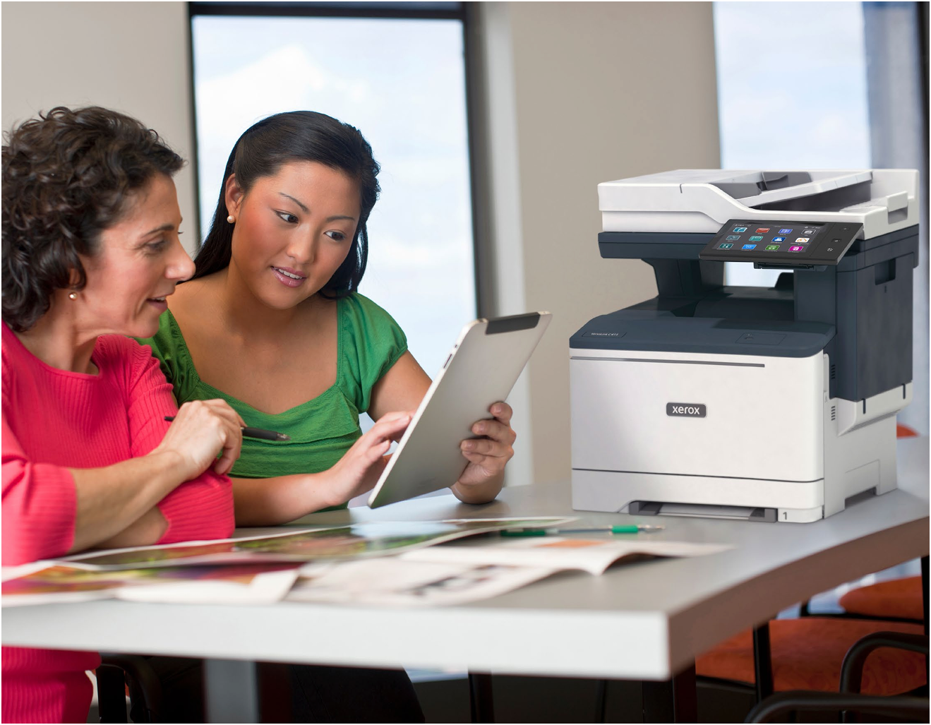 Two coworkers reviewing a tablet beside a printer in an office meeting room