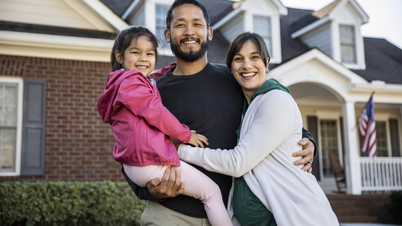 family of three smiles in front of their home that has home insurance