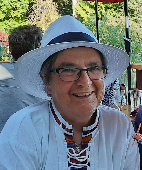Person wearing a white hat and glasses, smiling, seated outdoors.