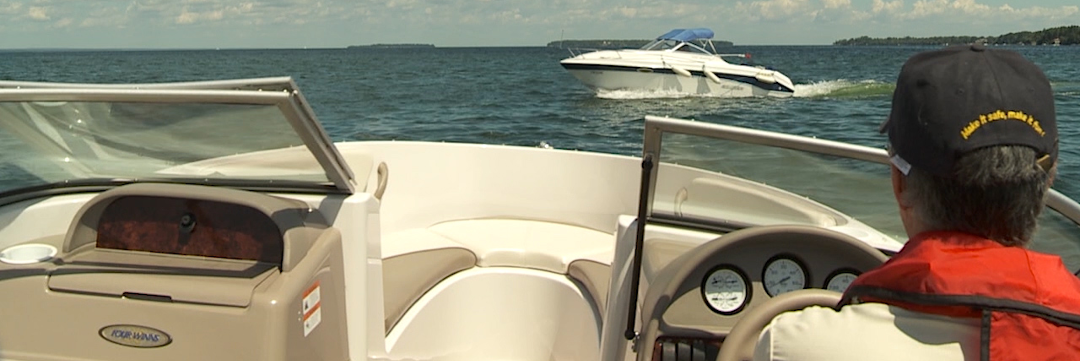 Boat on water with person in the driver's seat and another boat in the distance.