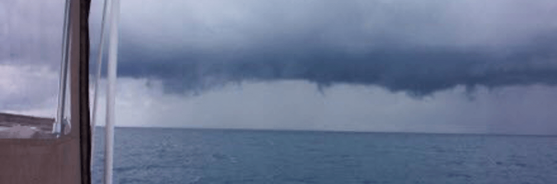 Dark storm clouds over the ocean, possibly rain in the distance. View from inside a boat.