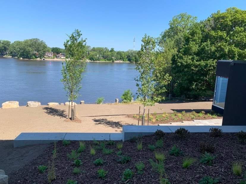 Vue sur le lac avec des arbres, une rivière et un bâtiment moderne par une journée ensoleillée.