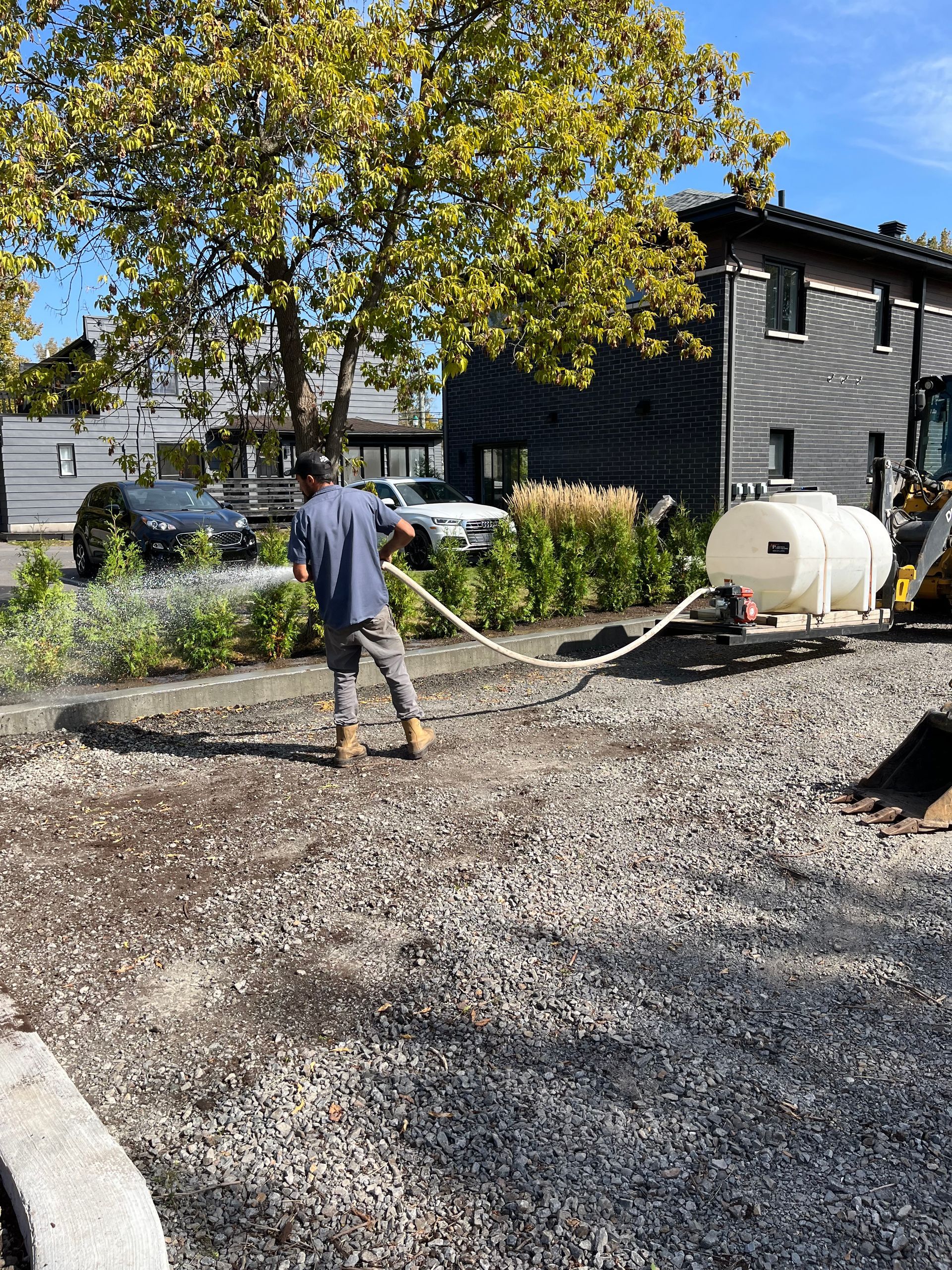 Un homme arrose du gravier avec une citerne, sur un chantier de construction.