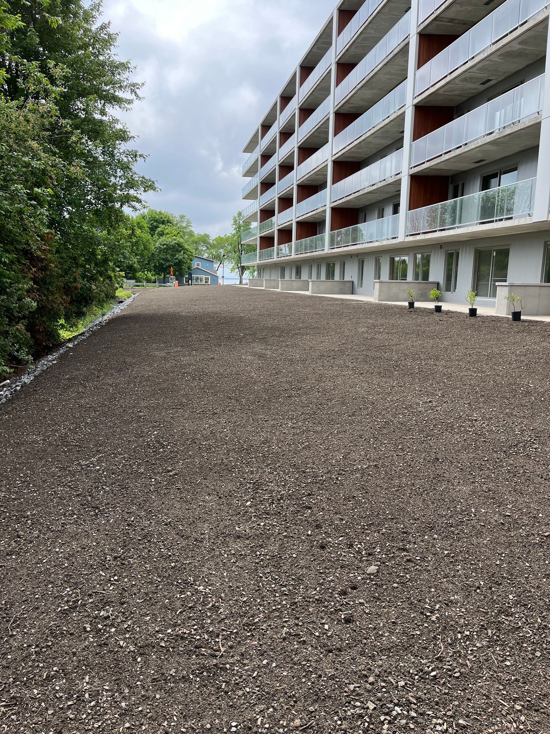 Une zone recouverte de gravier devant un immeuble de plusieurs étages avec balcons ; des arbres sur le côté gauche.