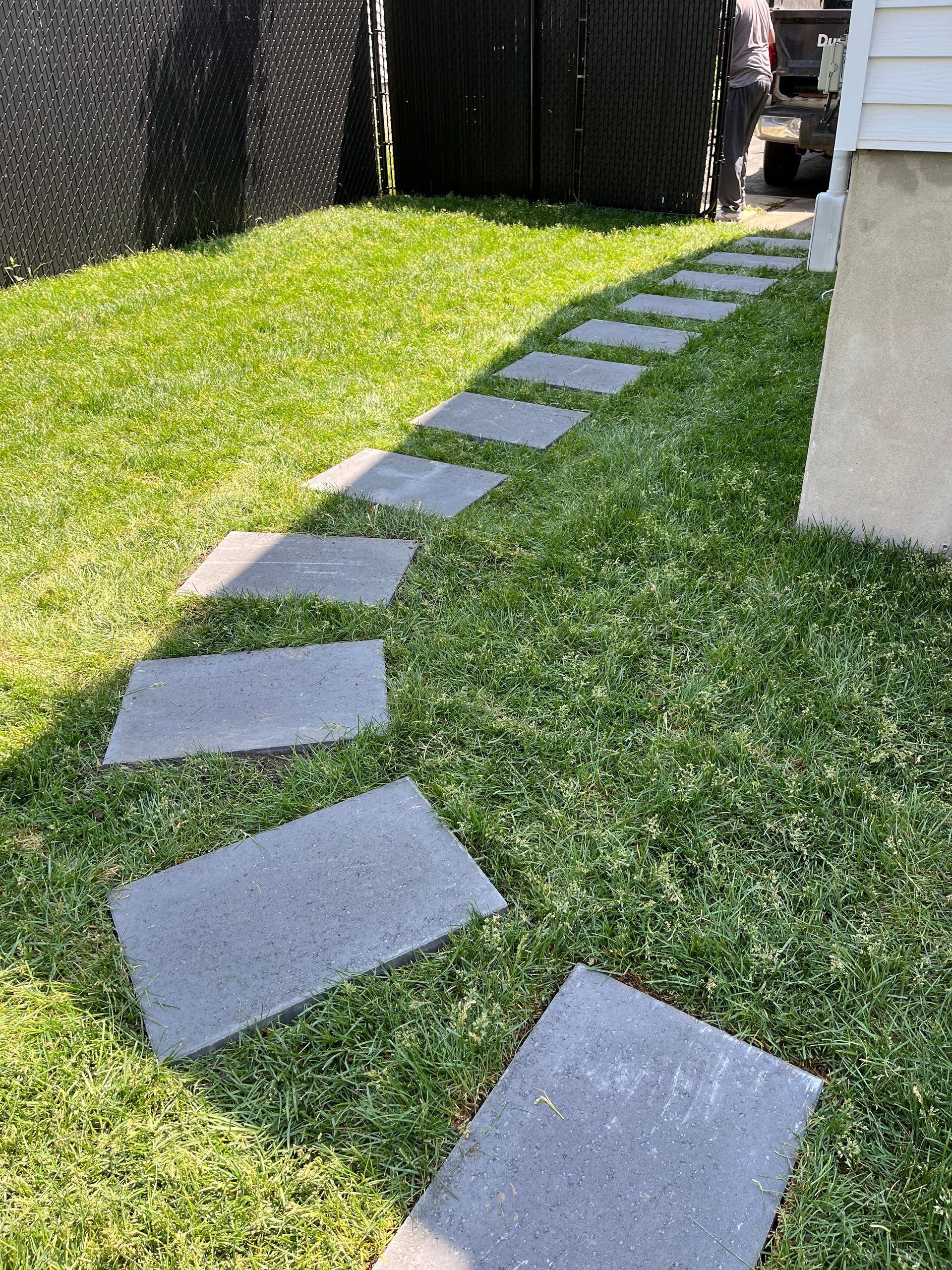 Des dalles de pierre dans l'herbe verte, menant à un bâtiment.