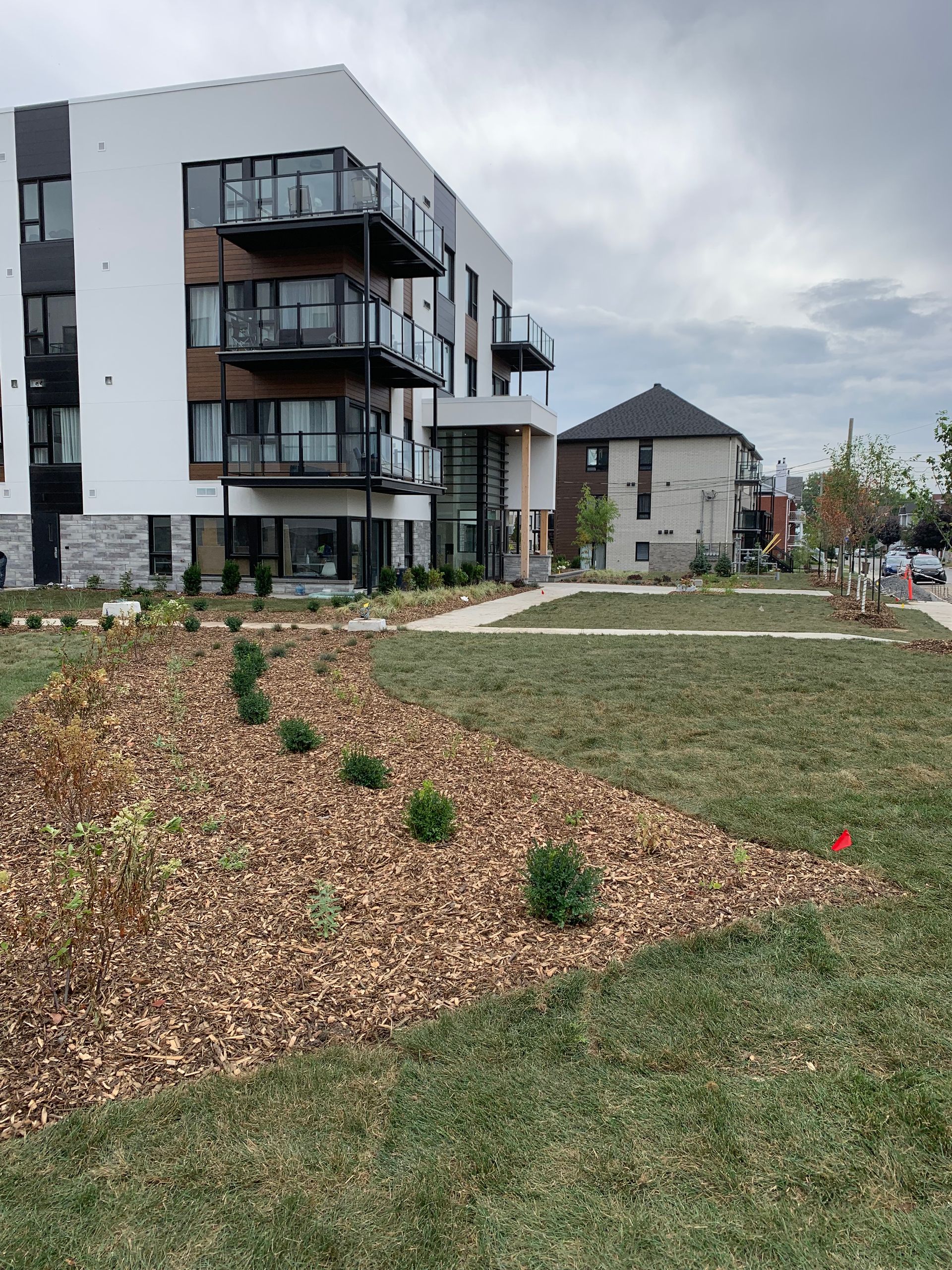 Immeuble d'appartements moderne avec balcons, jardin gravillonné et espace gazonné.