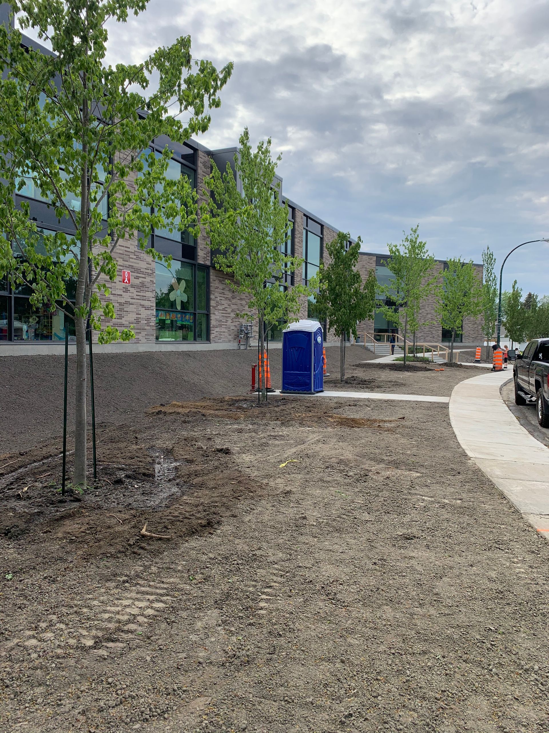 Vue extérieure d'un bâtiment avec des arbres et des toilettes portables par temps nuageux.
